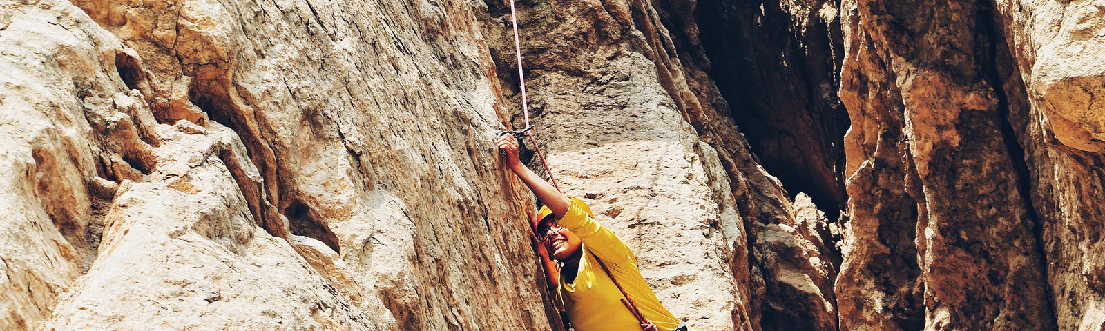 A woman climbing up a rocky cliff hangs from a rope, her face gritted with determination.