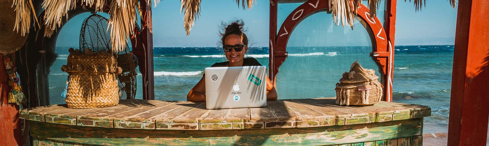 Digital Nomad (Remote worker) sitting in tropical hut with a beach and ocean in the backdrop.