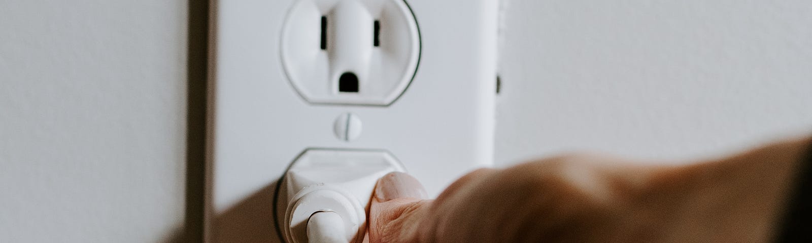 A hand removing a plug from a wall socket