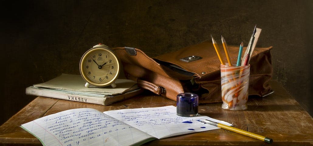Brown wooden desk with satchel, clock, pens, and writing book on it