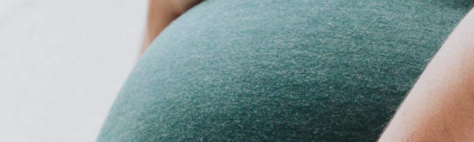 The torso of a pregnant woman wearing a green dress. She is using both hands to hold her belly.