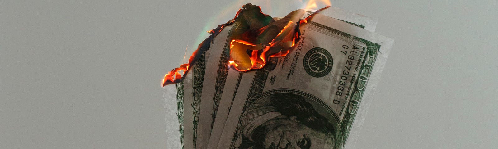 Someone holds up a handful of American currency. The bills are on fire.