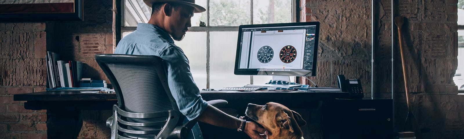 Man sitting at office desk petting big brown dog under his chin.