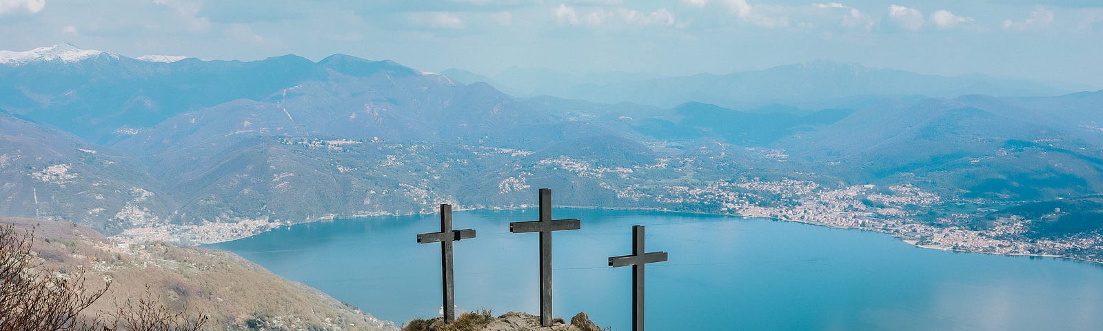 Three crosses on a sandy mountain overlooking a large body of bright blue water on a sunny day.