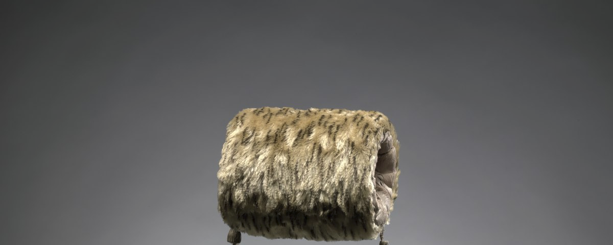 A photograph of a light brown and dark brown striped patterned faux fur muff with a gray background.