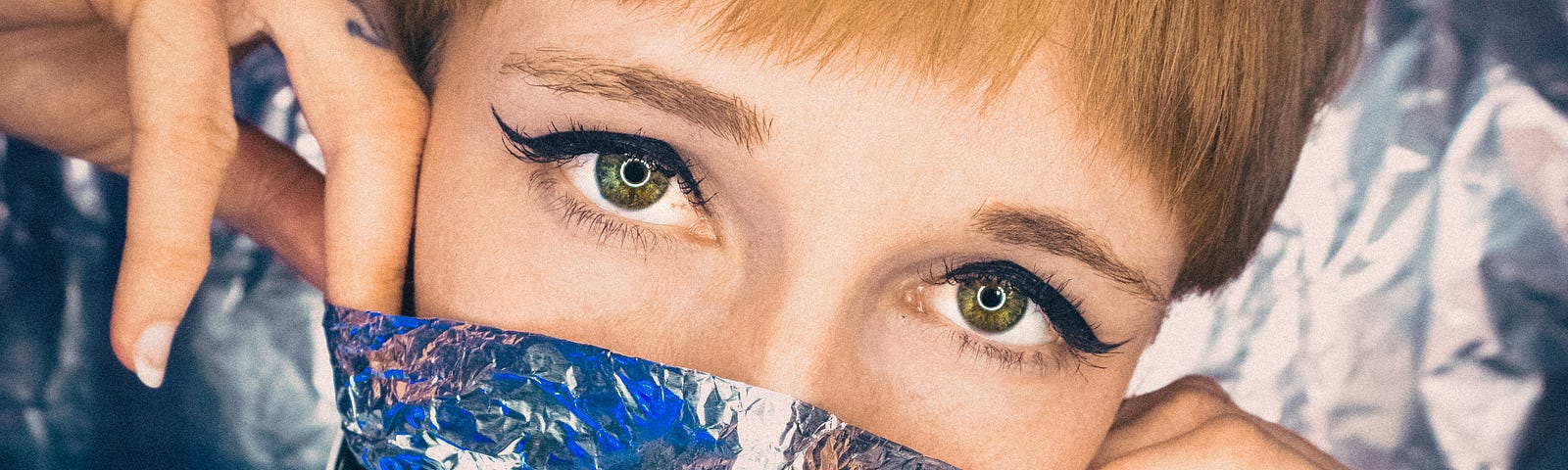 A woman holding aluminum foil across her nose and mouth like a mask.