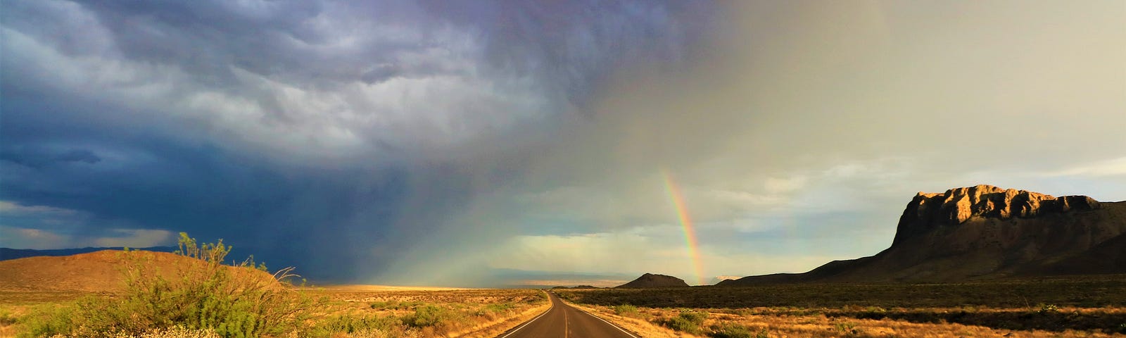 road with storm and a rainbow in the distance