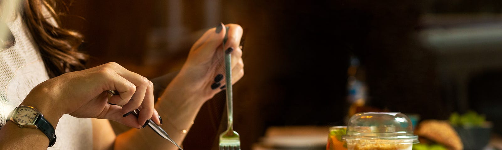 a woman’s hands holding a fork and knife, digging into a bowl of greens