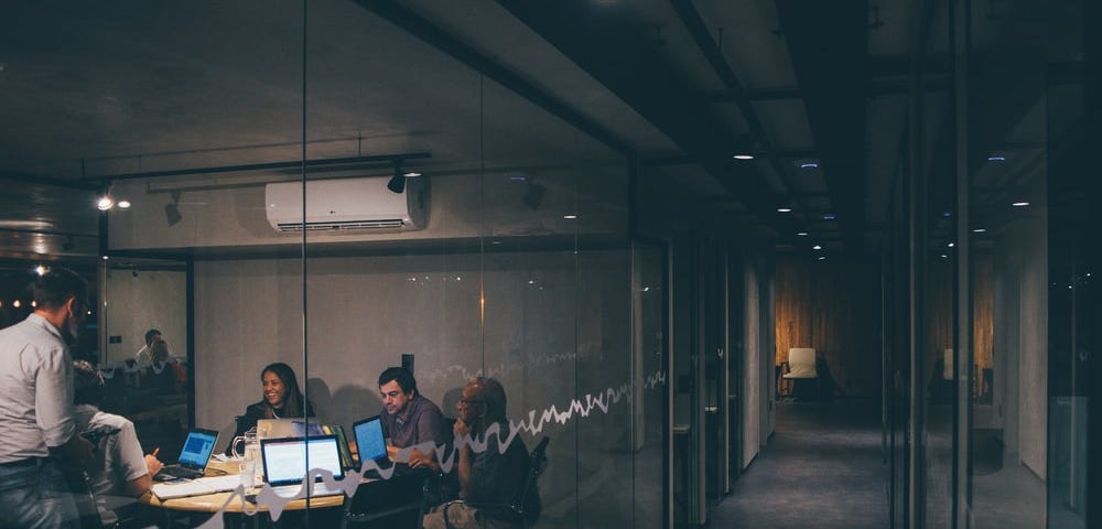 people working together on computers in a meeting room at night