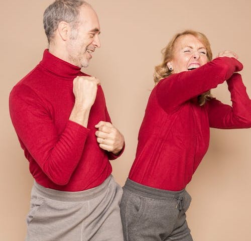 Cheerful mature couple dancing and laughing against beige background