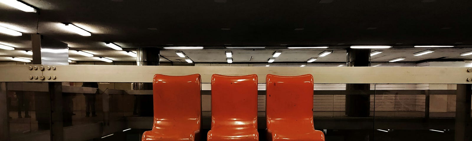 three empty orange chairs in a public place