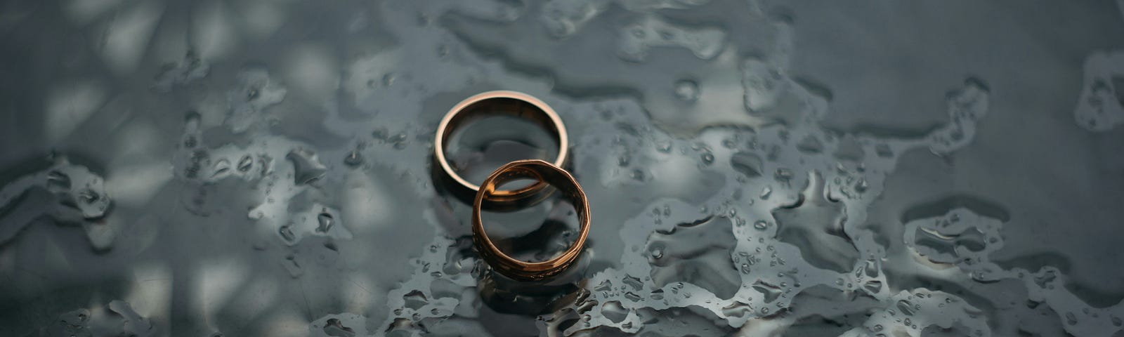 Two wedding bands laying on top of a wet surface.