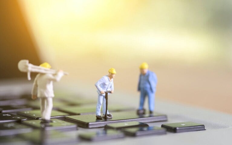 3 figurines of male construction workers wearing yellow hats, standing on a black computer keyboard