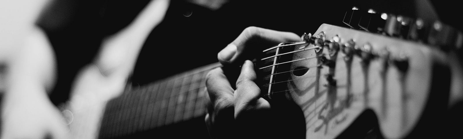 Someone playing an electric guitar, the neck and head in focused close-up, the other hand and body out of focus