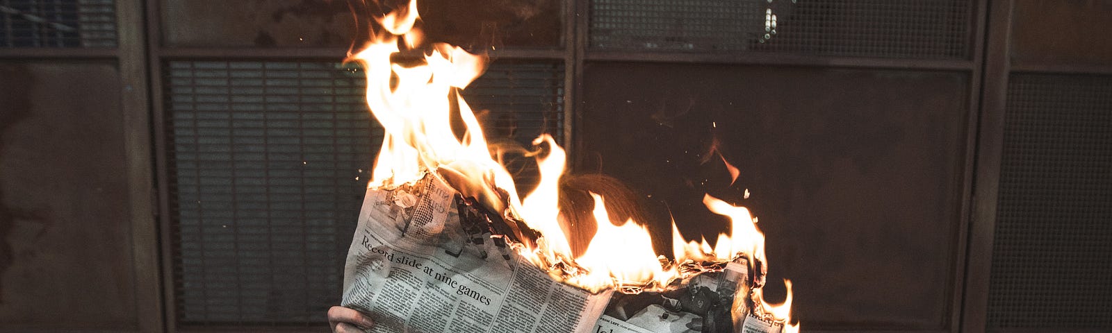 A man on a backwards chair holding a burning newspaper.