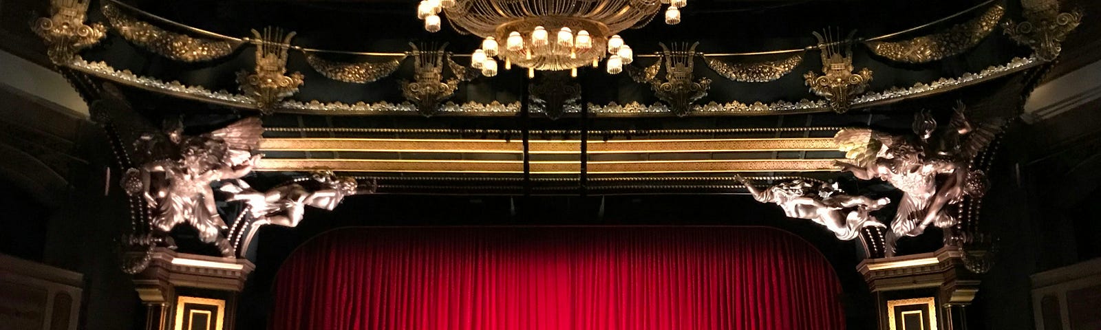 The red velvet curtains are closed over an ornate cinema screen