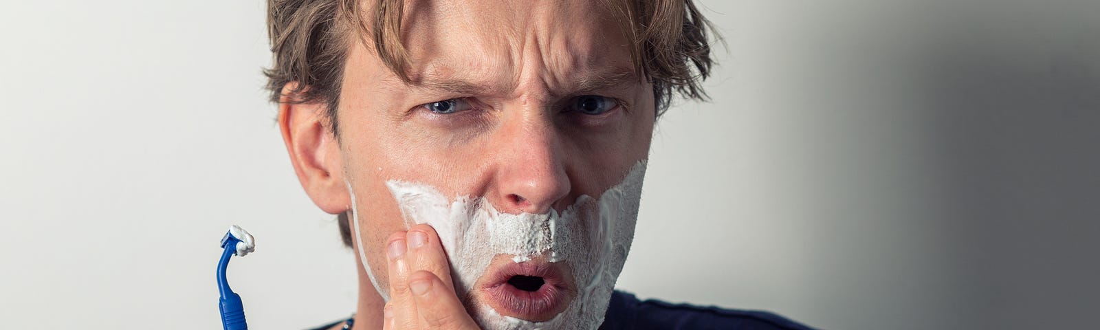 A man with shaving cream on his face, accidentally having cut himself.