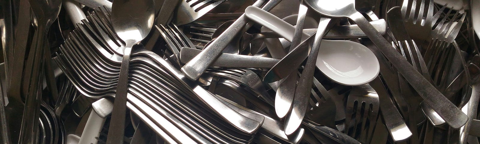 A haphazard collection of assorted cutlery, including plastic soup spoons and metal spoons and forks