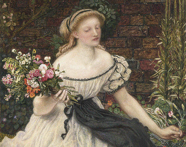 A painting of a young woman with blonde hair tied with a black ribbon sitting on the ground in front of a brick wall. She is in a garden wearing a cream colored gown, a black scalloped edged apron with black lace around the neckline and accents on short puffy sleeves. She is holding a bouquet of flowers in one hand and holding a flower in the other hand. There is large calico cat with wearing a black ribbon around its neck that is nuzzling against the woman’s gowned leg.