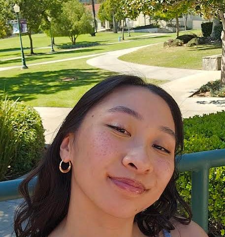 Image of 22 year old Meylina Tran, wearing a baby blue tank top, with the grass behind her, smiling at the camera.