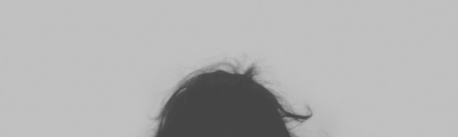 Black and white photo of back of woman with head bowed, in wind.