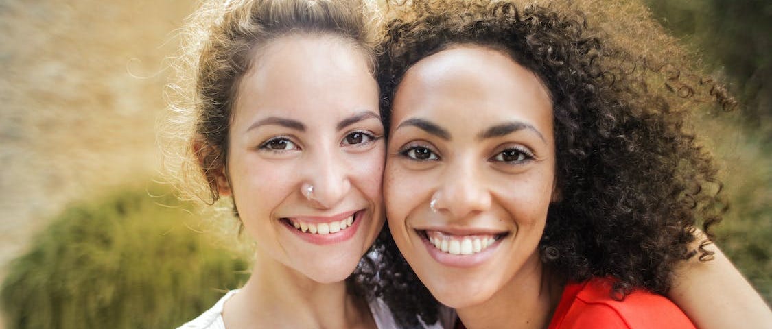 Photo of two smiling women leaning on each other and looking into the camera