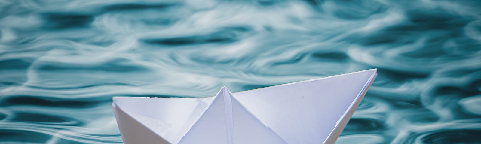 Folded paper boat floating in clear blue water
