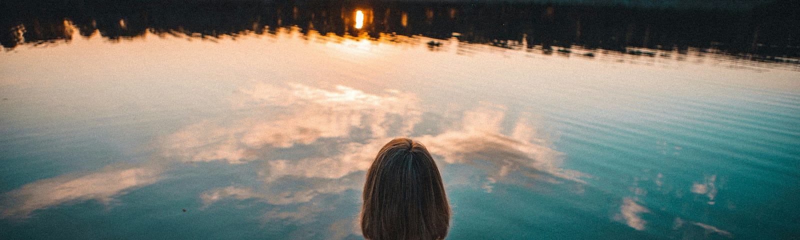 Woman sitting at the side of a pond staring at the sunset and contemplating life