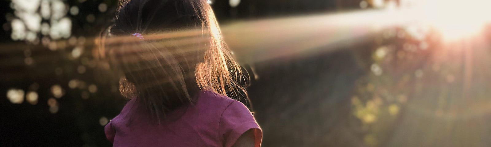 A young girl sitting amongst a field of clover looking at the sun.