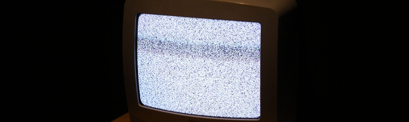 A vintage TV set on a small wooden table in a dark room. It only shows static.