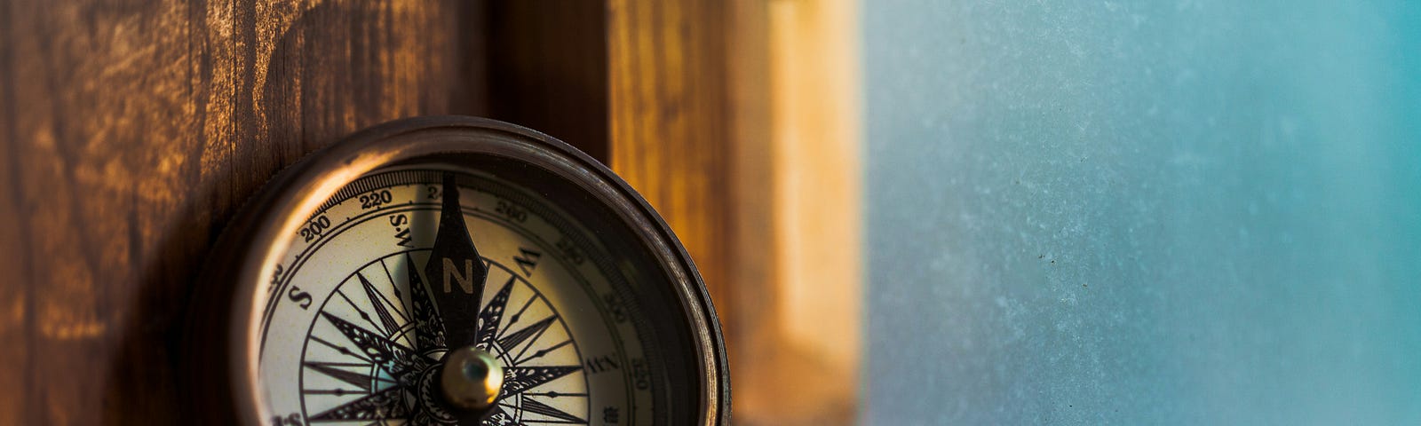 an antique compass, open leaning against an old wooden window frame.