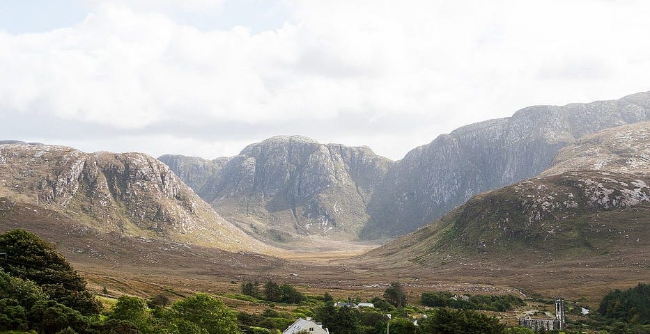 A lush green Irish valley with trees and houses, surrounded by brown treeless mountains