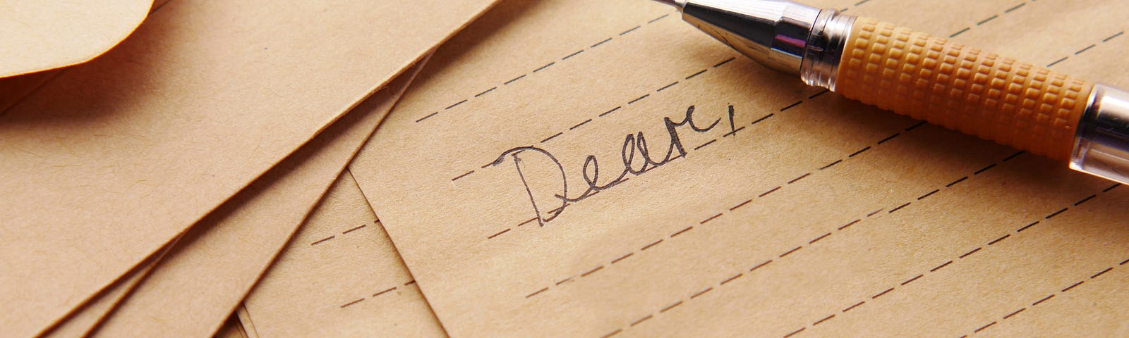 Image of a pen and paper with the greeting “dear” written.