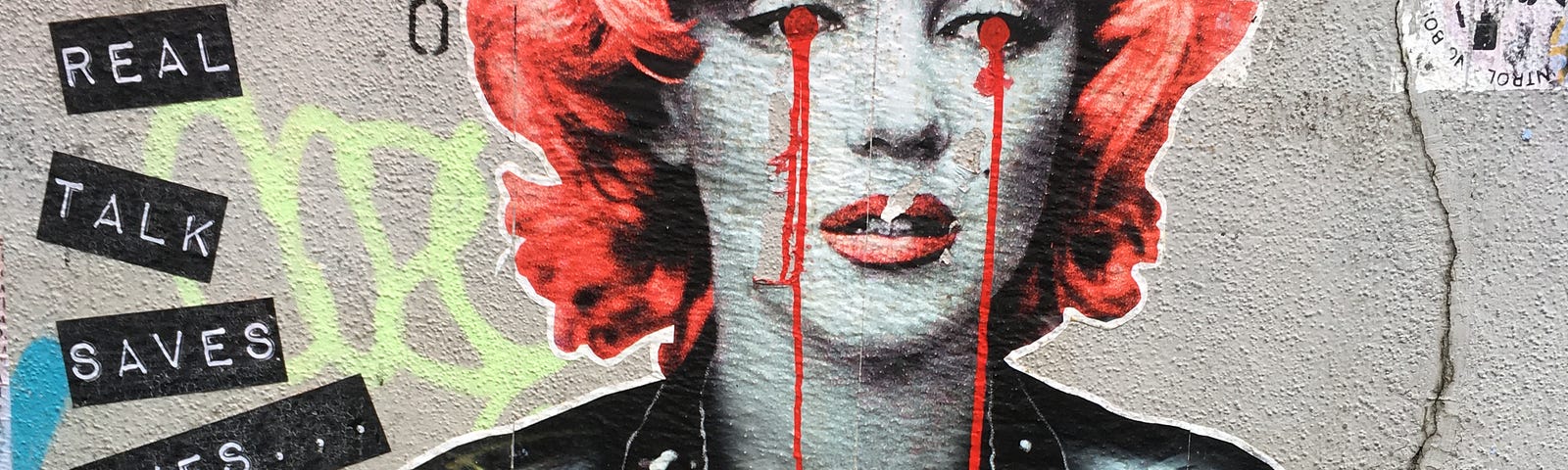Graffitti wall of Marilyn Monroe with red tears running down her face. With words “Real Ralk Saves Lives”.