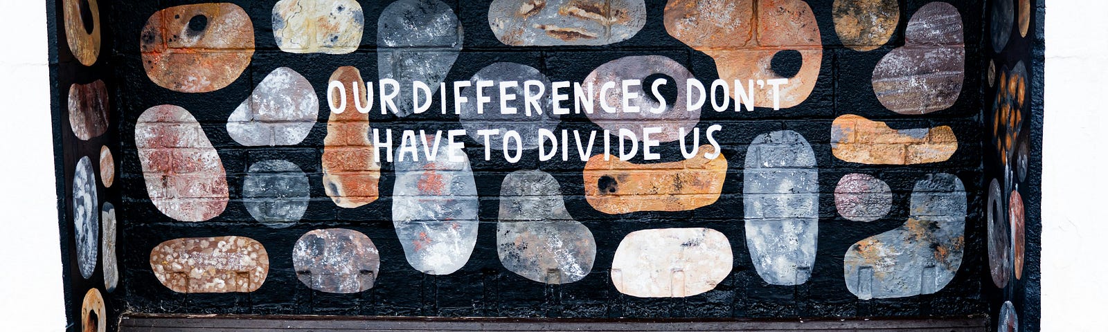 A mural behind a bench of different coloured and patterned shapes with text over that says “Our differences don’t have to divide us”.