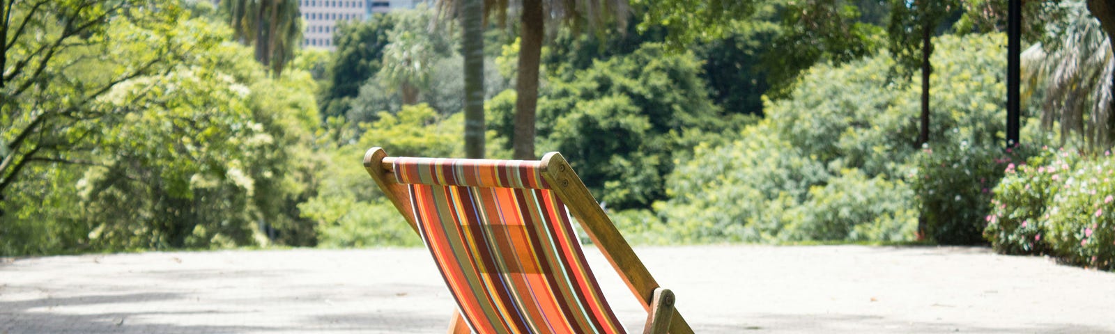 An empty orange and black stripped fold-up chair in a city park, waiting for someone to sit in it.