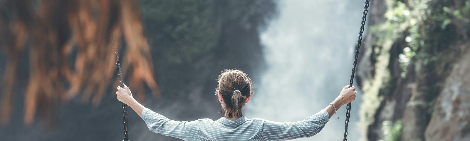 A woman sits on a swing looking at a vast waterfall