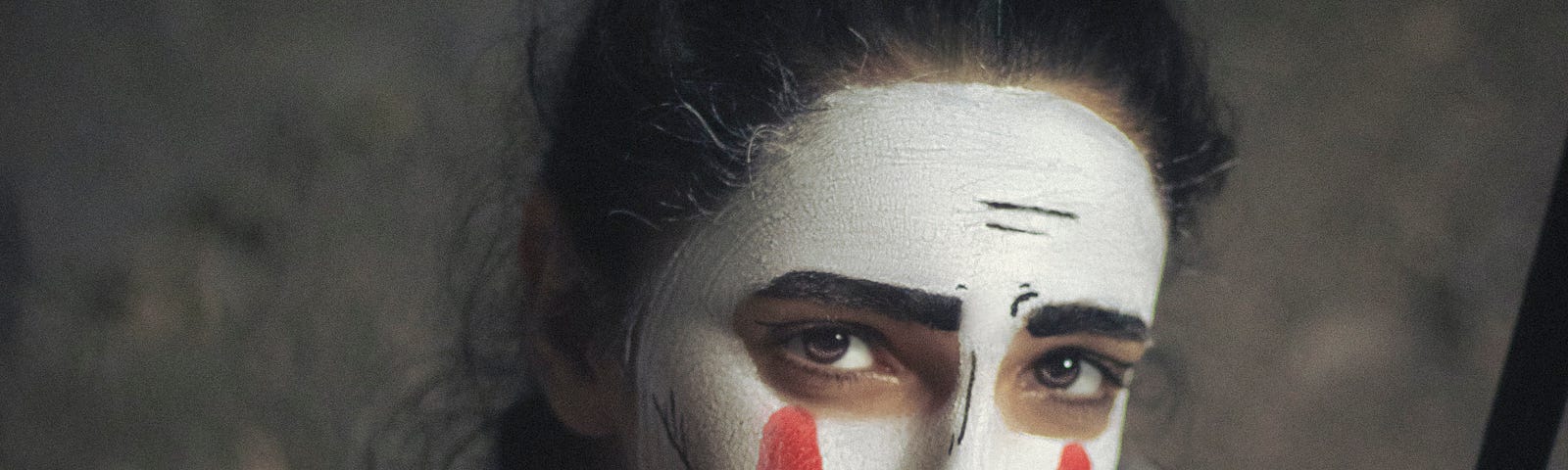 Person in mime make-up drawing red tears down their face