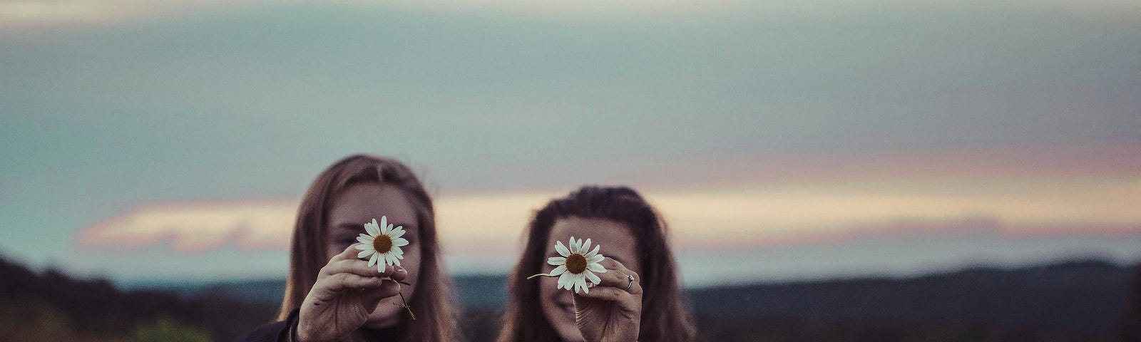 two women holding flowers up in front of their faces while standing outside