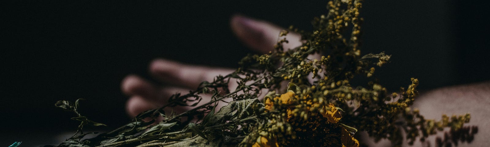 Hand lying down on a floor against a black background. Yellow flower is in front of the hand.