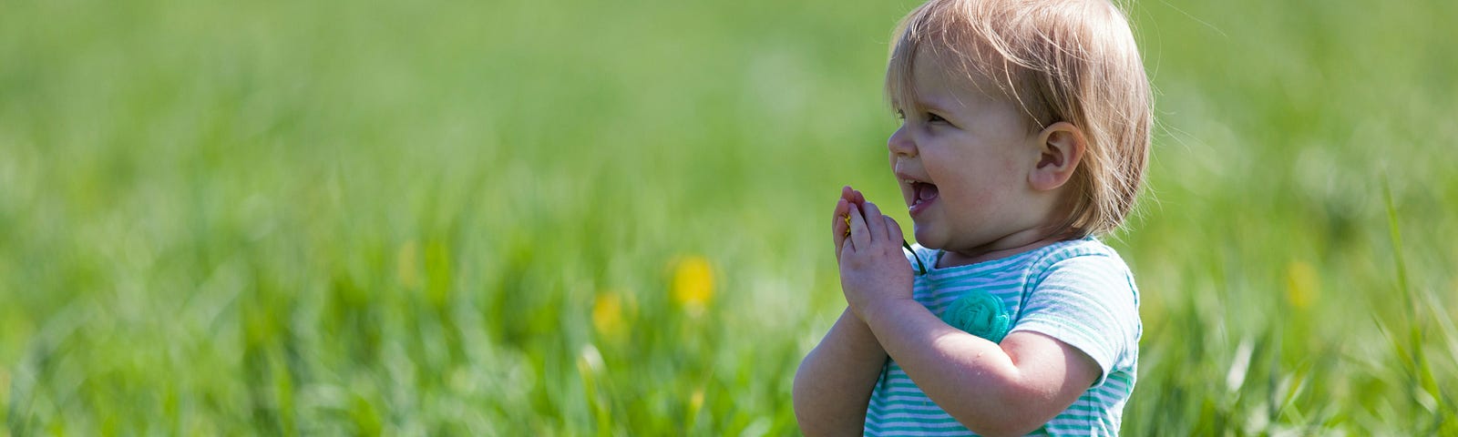 Young child in a grassy field laughing and clapping