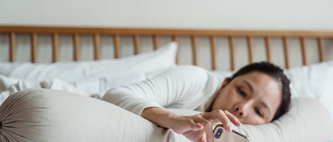 Lazy blogger woman using smartphone in bed