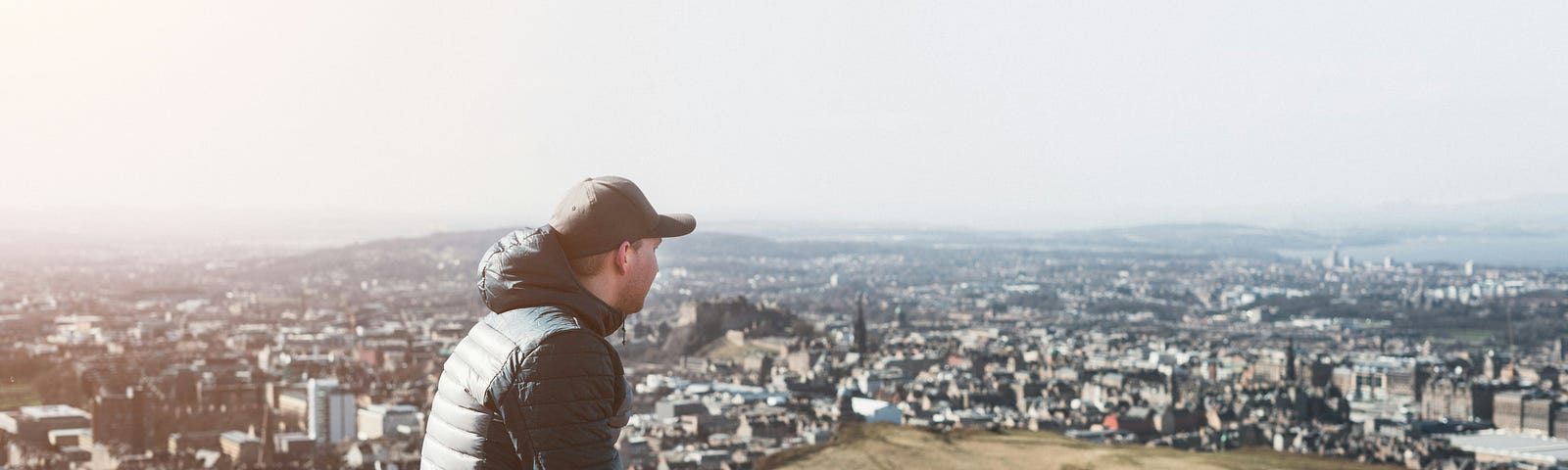 Man sitting on a rock overlooking the a city in the distance.