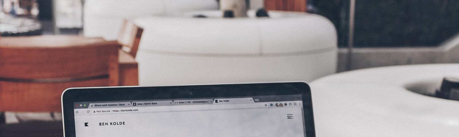 A laptop on a wooden desk and the screen is showing a black text on a white background, saying ‘I design and develop experiences that make people’s lives simple’.