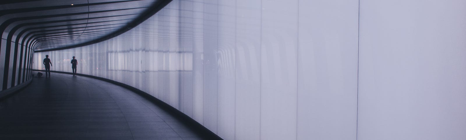 A curved hallway, with the dark silhouettes of two people in the distance.