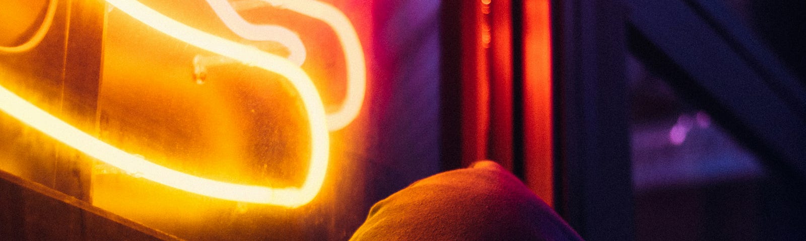 A man stands in front of an illuminated hot dog sign at night.