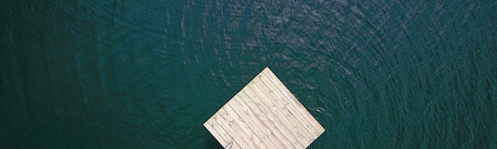 A bird's-eye view of a wooden raft floating on dark-blue water.