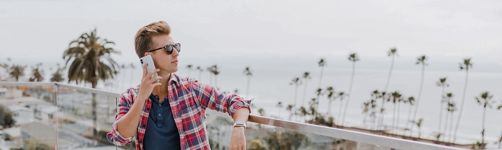 A guy in a balcony overlooking a beach while on his phone