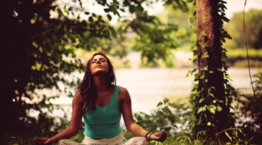 Woman sits to meditate in nature near trees and water