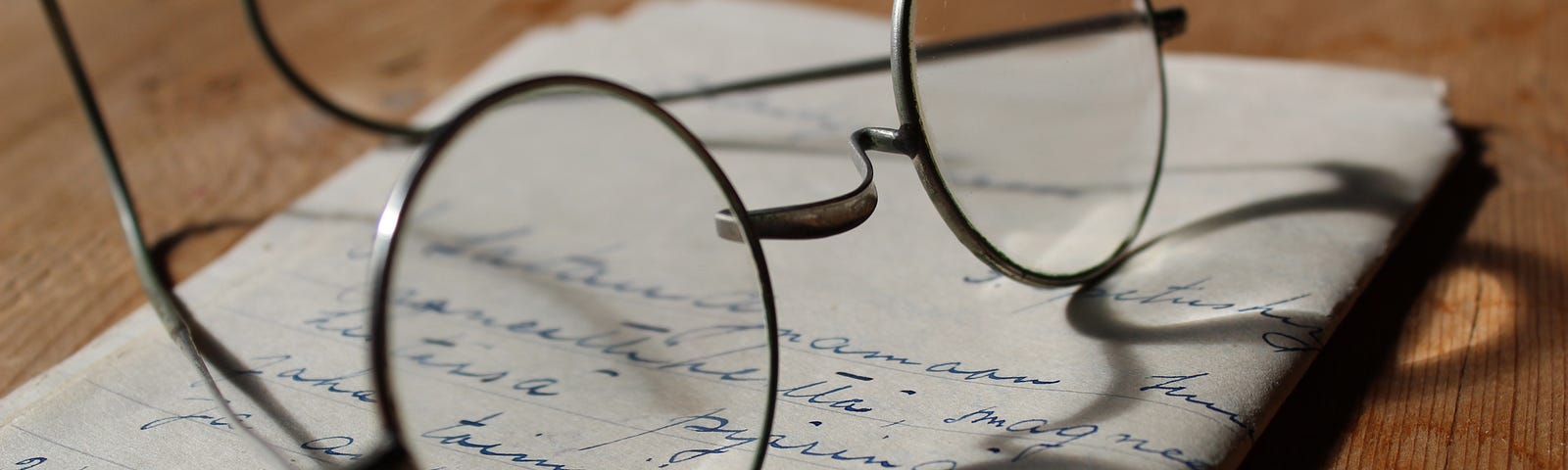 An image of a folded piece of paper on a wooden surface, words written on it and glasses lying on top of it.